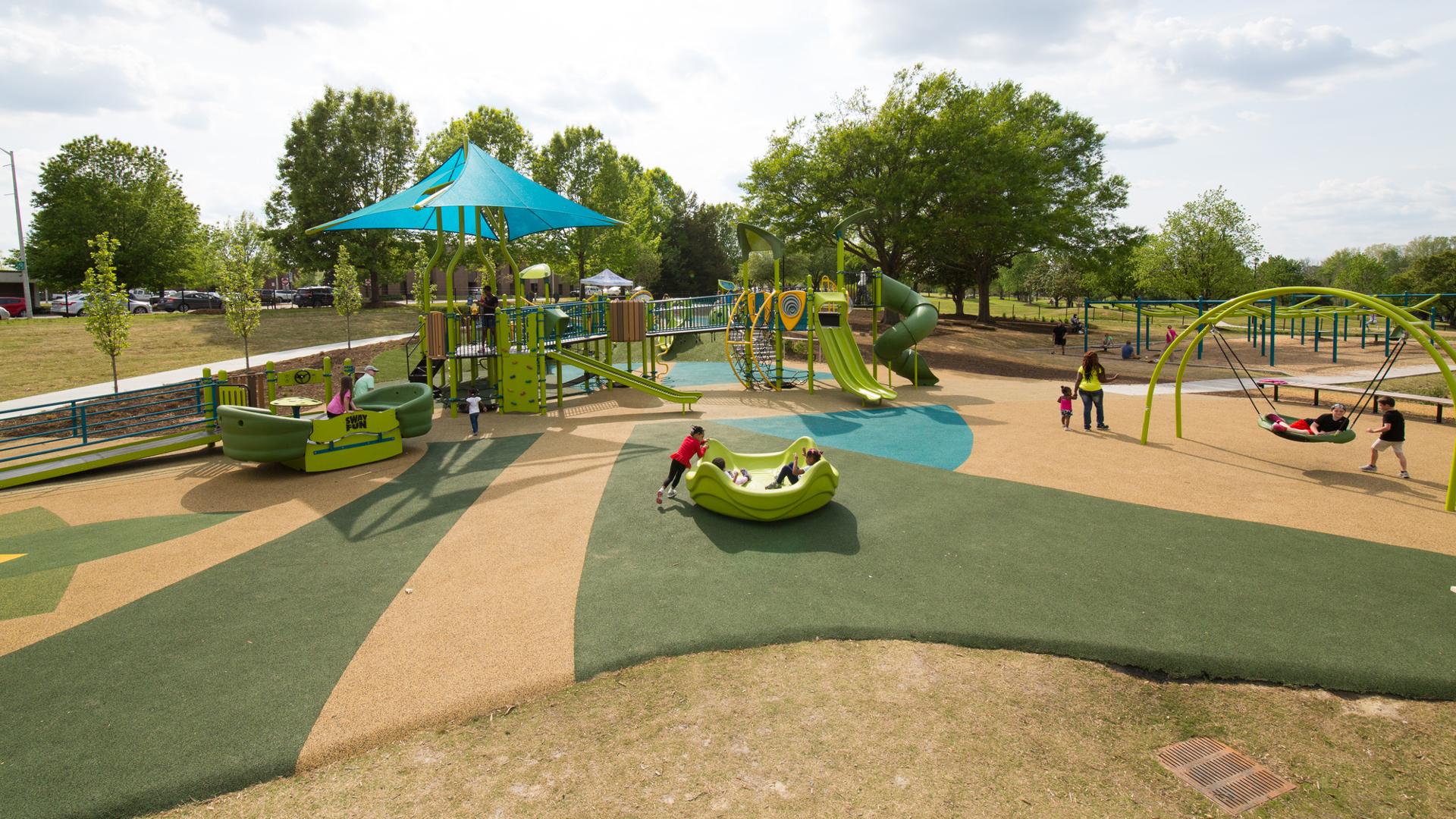 Three kids play in an Omnispin, while a mother takes her daughter for a walk. Two boys play on an Oodle Swing.