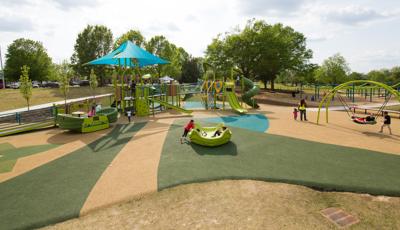 Three kids play in an Omnispin, while a mother takes her daughter for a walk. Two boys play on an Oodle Swing.