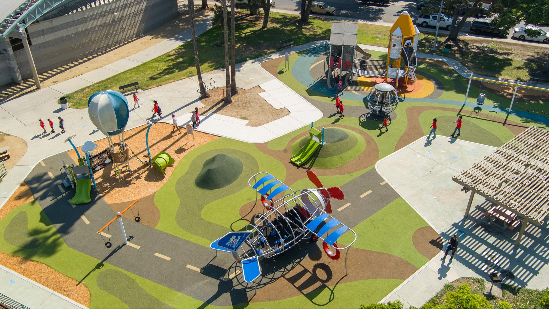 Elevated view of children playing on a playground themed with play structures shaped like an airplane, hot air balloon, and a rocket ship.