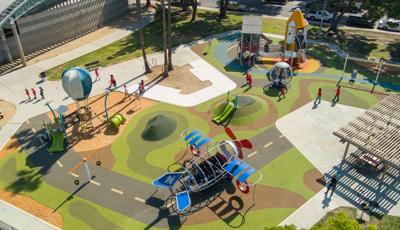 Elevated view of children playing on a playground themed with play structures shaped like an airplane, hot air balloon, and a rocket ship.