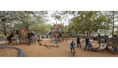 Families enjoy this nature-inspired playground. A father helps his toddler down a PlayShaper slide. A group of older kids play on the Geoplex net structure.