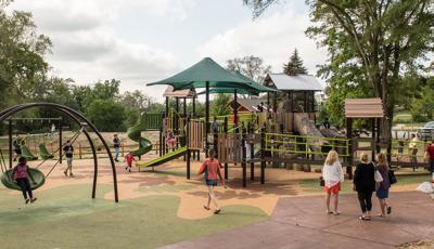 This naturally-themed playground is full of children of all abilities accessing this playground's amenities. A girl sits on the Oodle swing. Parents enjoy the Sway fun and kids use the different ramps to get from one place to another.