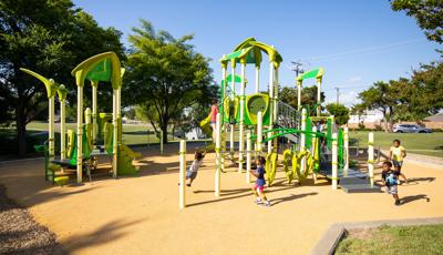 Children running and playing around two play structures with bright green climbers and slides with unique triangular shaped roofs.