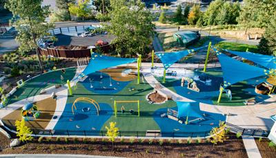 A large playground made up of smaller inclusive play activities with big fabric shade sails over the equipment. 