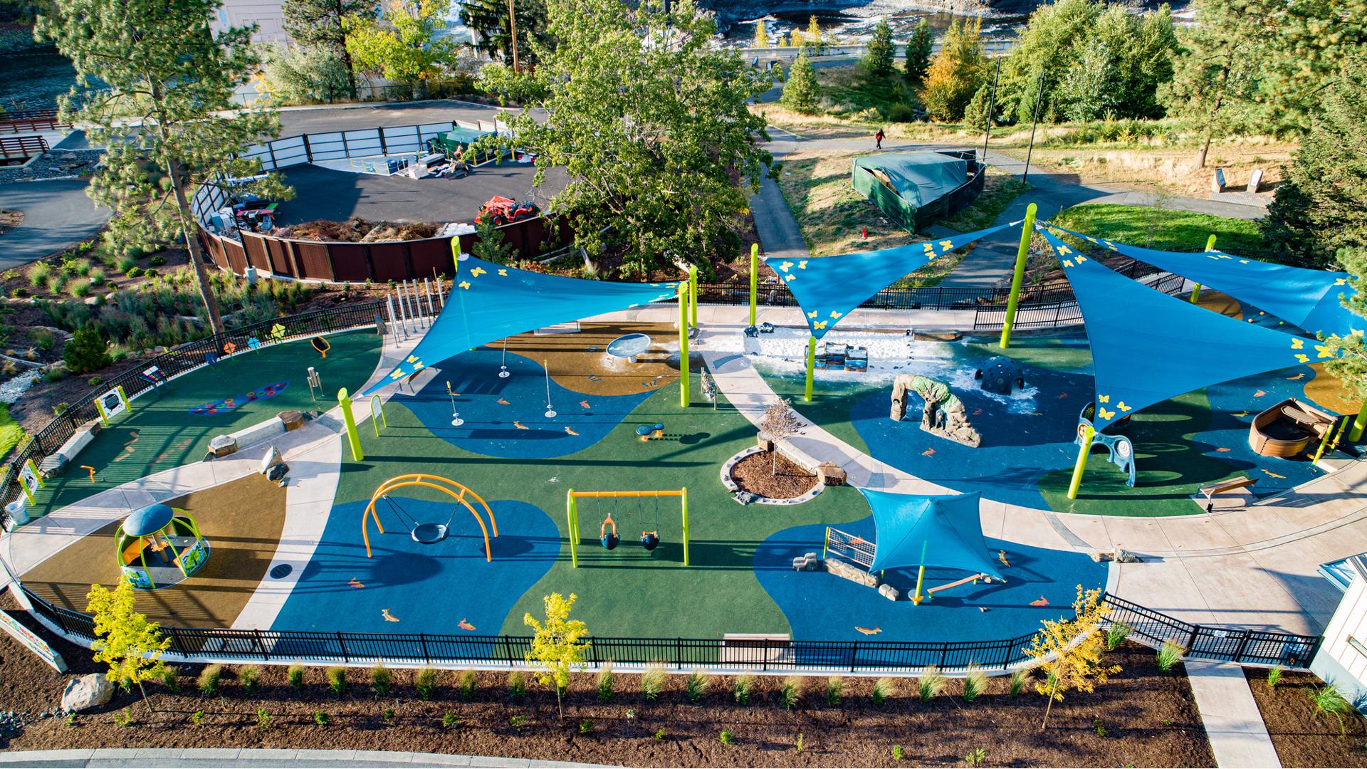 A large playground made up of smaller inclusive play activities with big fabric shade sails over the equipment. 
