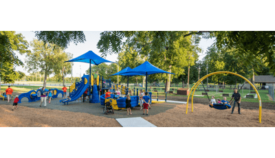 A dad pushes kids on a Oodle swing as ther families play on the playground.