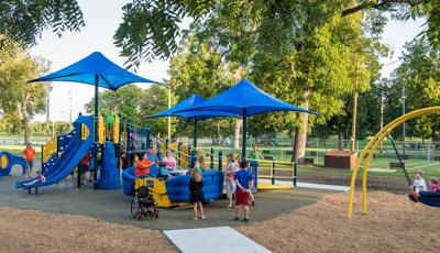 A dad pushes kids on a Oodle swing as ther families play on the playground.