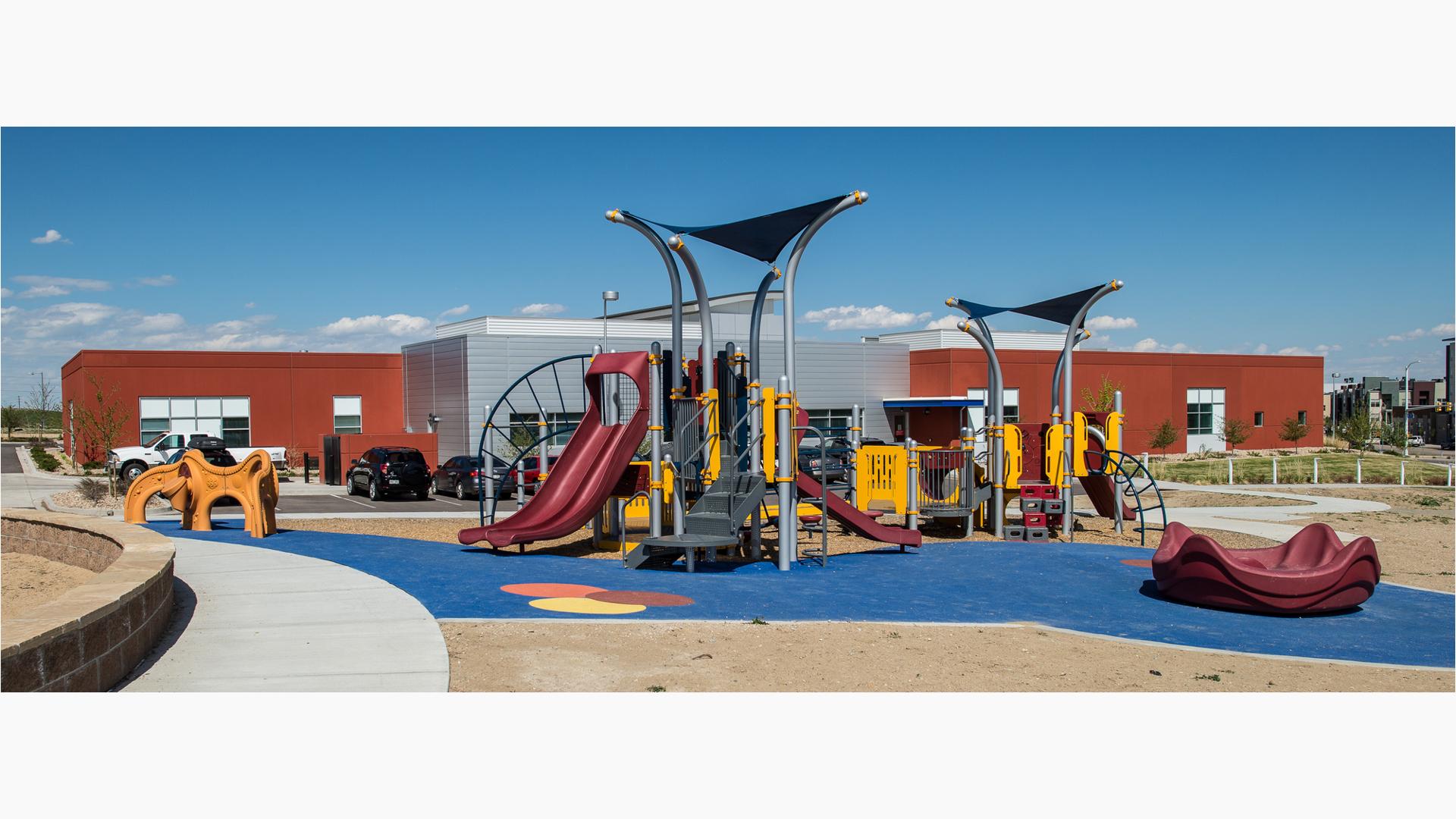 Red, silver and yellow playground in front of red and silver building. 