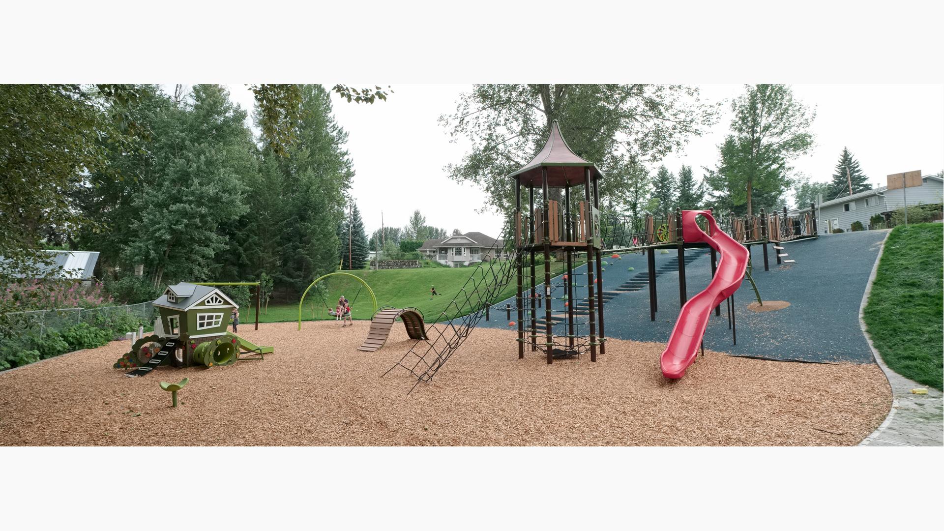 A tower structure accessible by a bridgeway cutting across a hillside also has a cargo net access from the ground. A second small house like play structure sits next to the tower. 