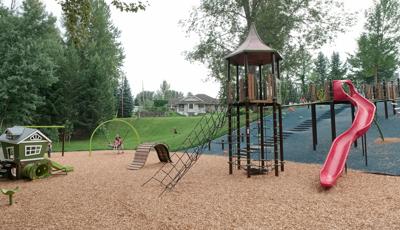 A tower structure accessible by a bridgeway cutting across a hillside also has a cargo net access from the ground. A second small house like play structure sits next to the tower. 