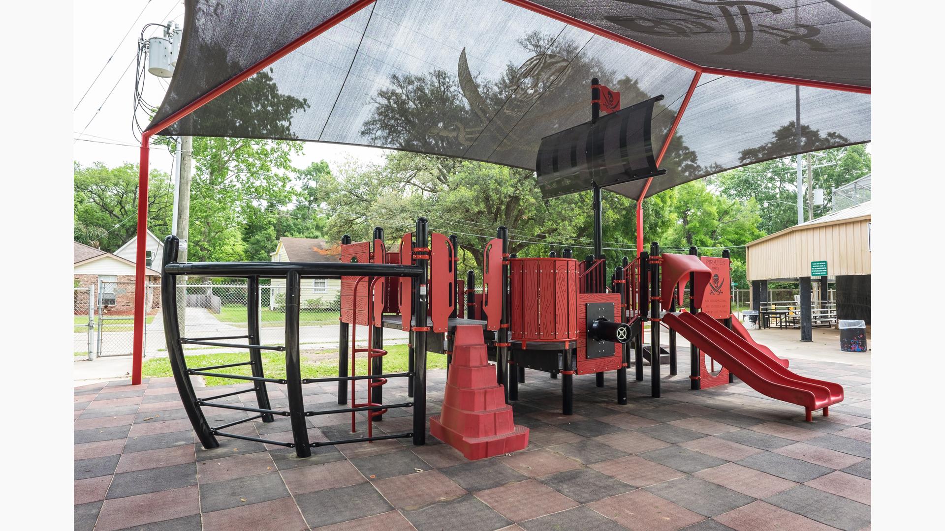 Custom pirate ship designed playground sitting under black skull with cross swords shade canopy.