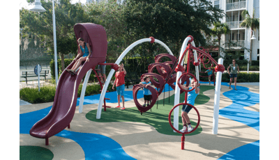 A manufactured surface on the ground. A girls rides down the Evos slide. Other kids play on the other parts of the structures as an adult looks on. 