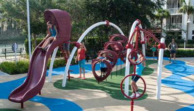 A manufactured surface on the ground. A girls rides down the Evos slide. Other kids play on the other parts of the structures as an adult looks on. 