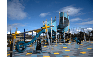 A open playground area with large tower and other surrounding play activities with the ground surfacing made of multi-colored square tiles.