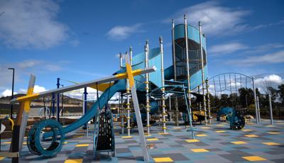 A open playground area with large tower and other surrounding play activities with the ground surfacing made of multi-colored square tiles.
