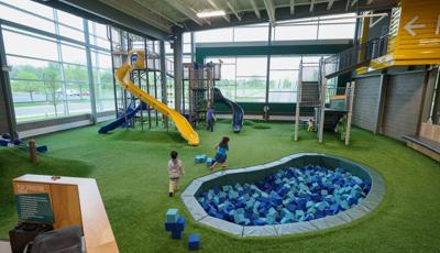 Indoor church playground featuring a tall yellow slide with a net structure and foam pit surrounded by grass looking safety surfacing and floor to ceiling windows.