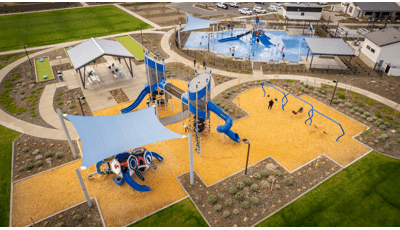 Elevated view of a playground play area with a covered picnic area and near by splash pad.