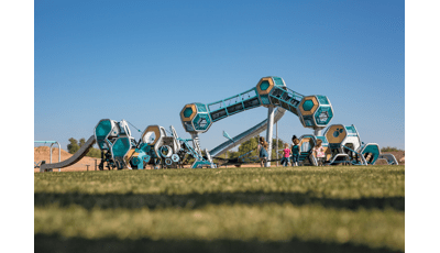 Three separate futuristic like play structures have hexagonal play pods all connected by climbers, slides, and belted pathways. One structure is three towers with a single hexagonal pod on the top, enclosed crawl tunnels connect the play pods.