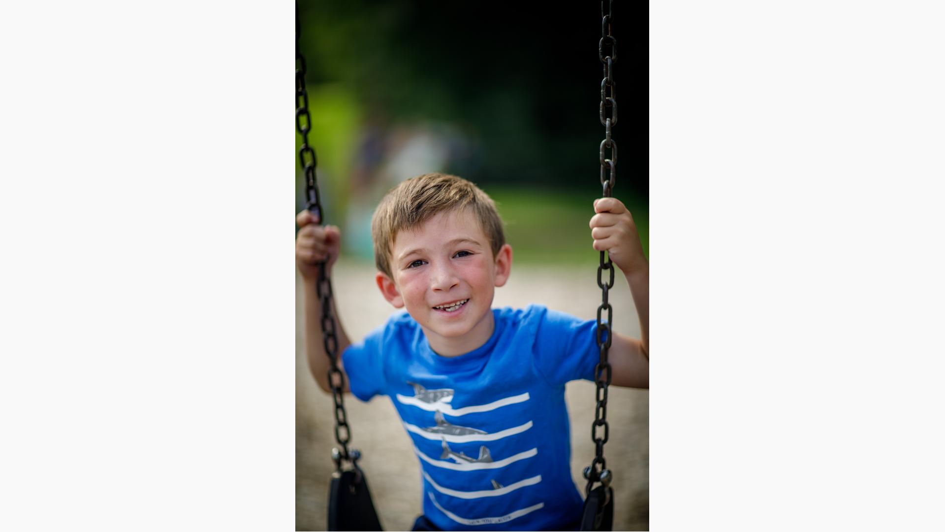 Boy in blue shirt smiles as he sits on swing