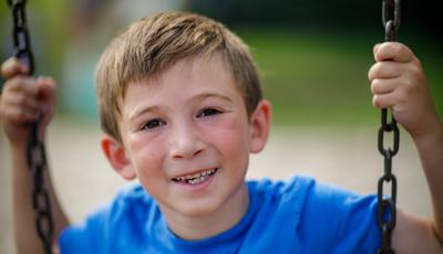 Boy in blue shirt smiles as he sits on swing