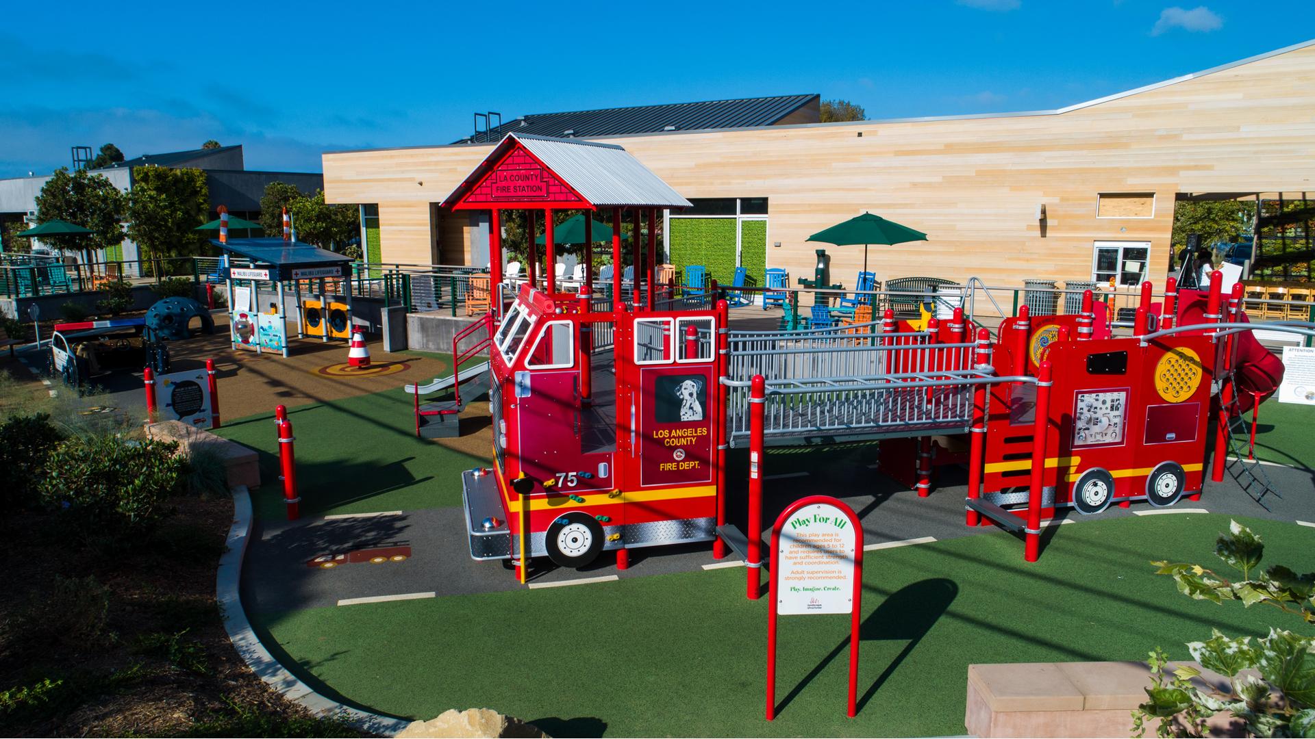Full elevated view of an inclusive play area with a large play structure designed like a fire engine driving down a road.