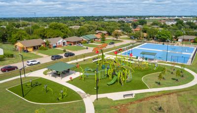 Elevated view of a neighborhood nature themed playground, outdoor work out equipment, and nearby basketball courts.