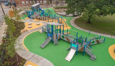 Elevated view of a outdoor play area with one play structure accessible by ramps and open playground decking, slides, climbers and play panels while the other has multiple unique rope climbers, ramps, slides, and play panels.