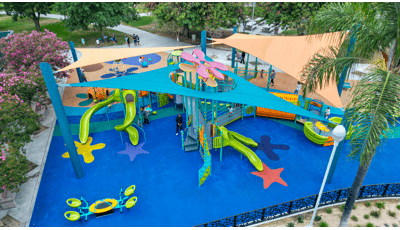 Elevated view of a ocean themed tower playground structure peaking through a port hole of a large shade system over the entire play area of the park.