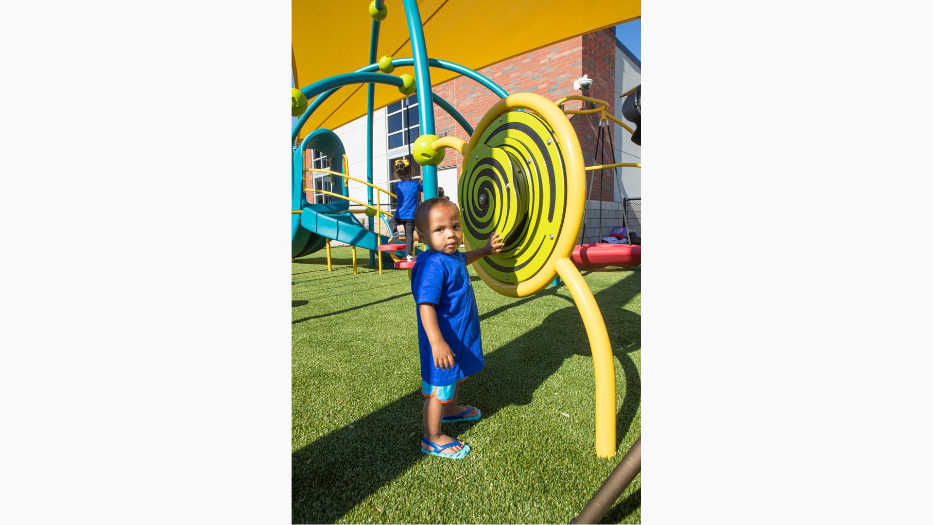 Boy in blue shirt and sandals playing with learning wall element