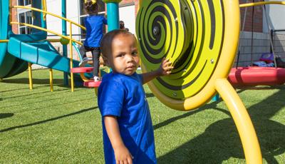 Boy in blue shirt and sandals playing with learning wall element