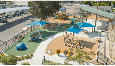 Elevated view of a park playground with scattered blue square shades covering different play areas.