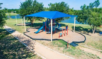 Elevated view of a large blue rectangular shade over a play structure all set next to a nearby lake.