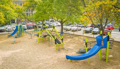 Elevated view of a city elementary school playground with three separate main play structures surrounded by mature trees and a parking lot.