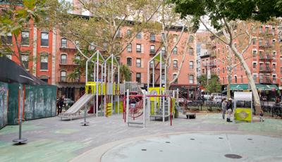 A silver and green color modern style play structure sits amongst older city brick buildings.