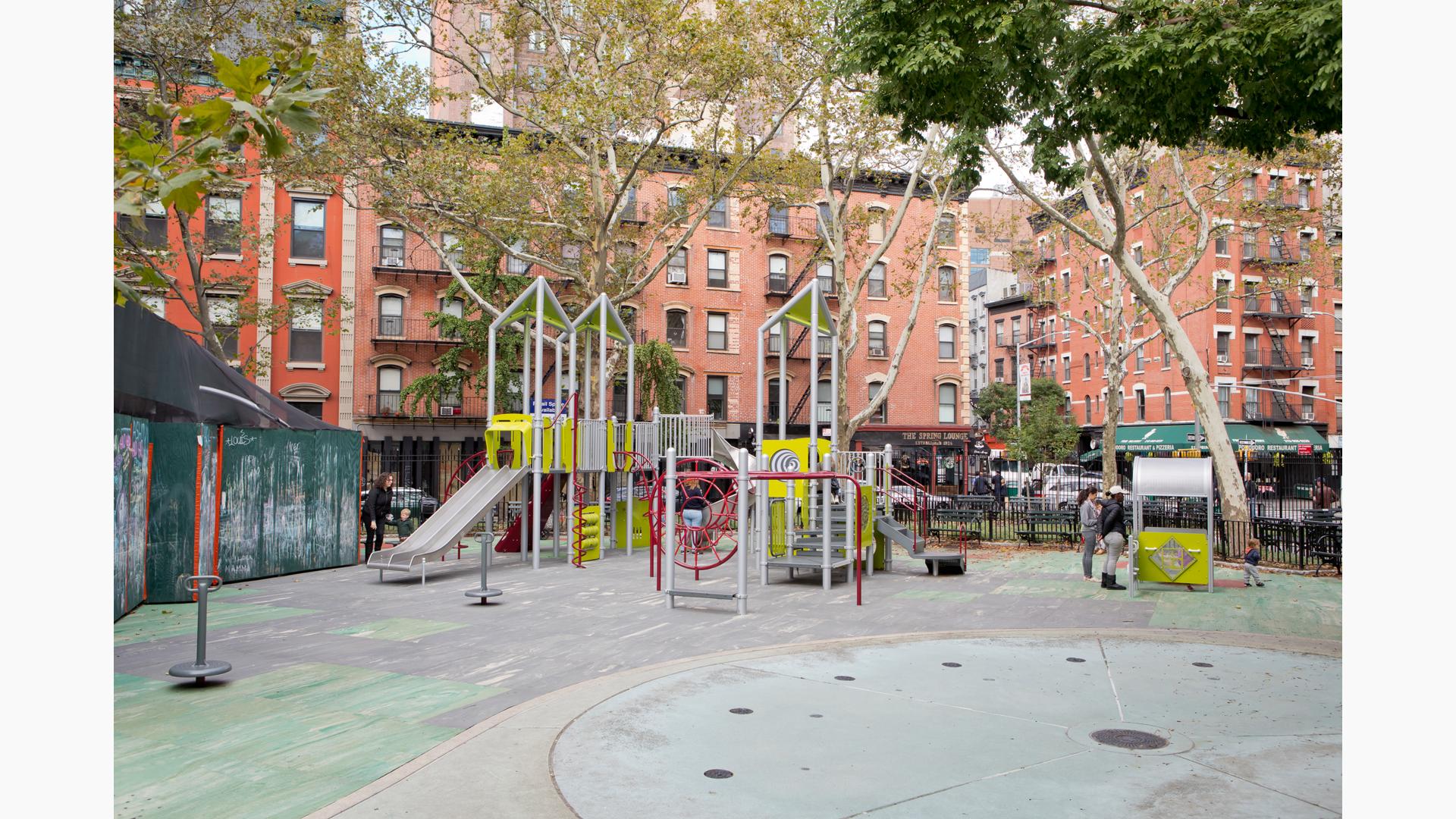 A silver and green color modern style play structure sits amongst older city brick buildings.