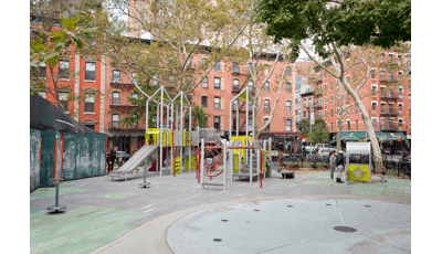 A silver and green color modern style play structure sits amongst older city brick buildings.