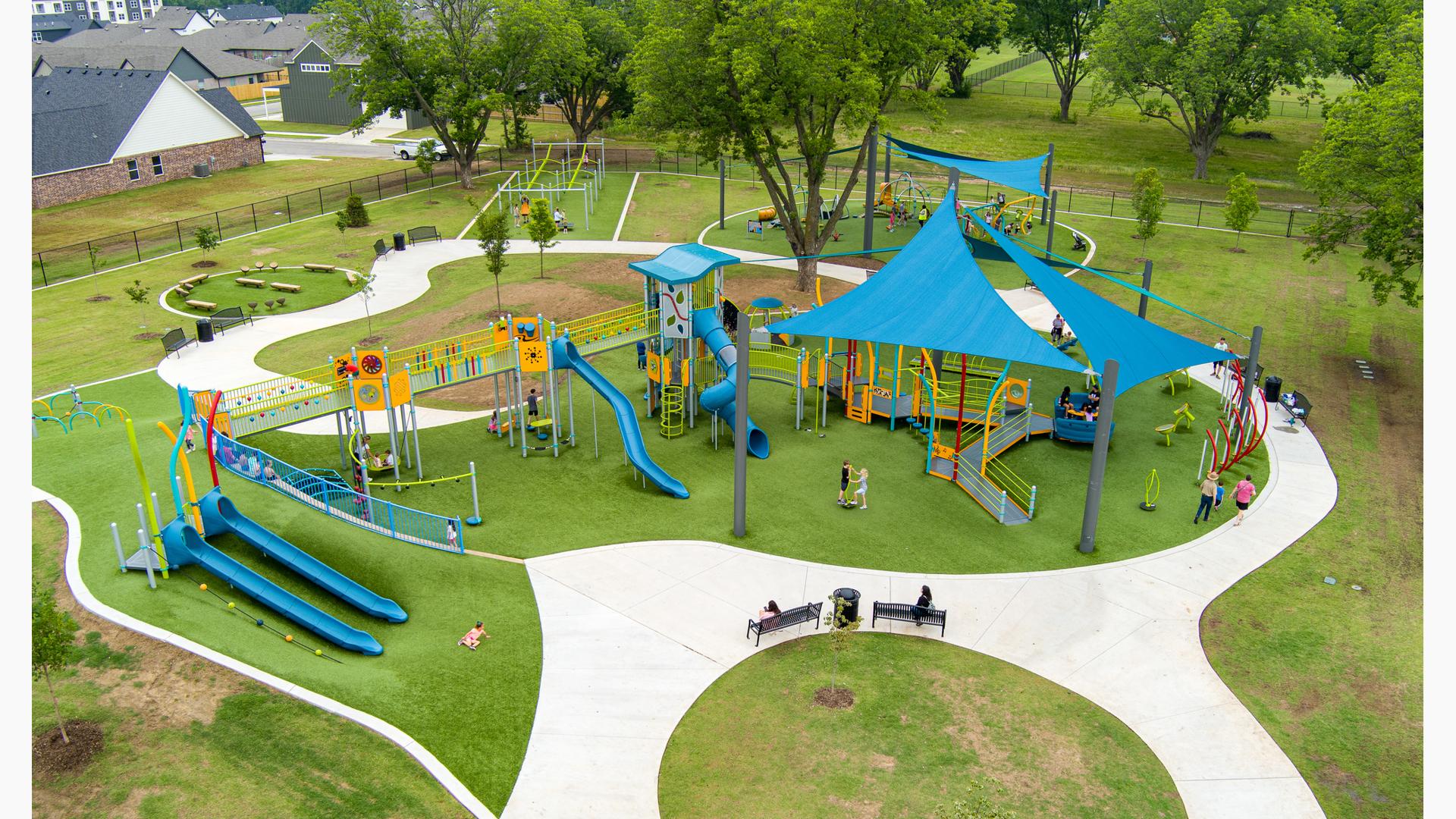 Elevated view of families playing at a playground with large blue shade sails overhead. 