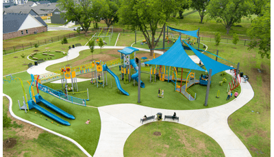 Elevated view of families playing at a playground with large blue shade sails overhead. 