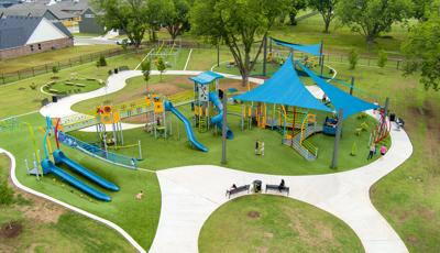 Elevated view of families playing at a playground with large blue shade sails overhead. 