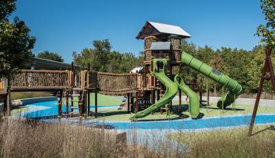 Surrounded my trees and tall grass, this marine-themed custom playground features concrete-sculpted crabs and custom TuffRiders® and DigiFuse® panels. The second play structure at this park is a custom nature-inspired PlayBooster® play structure that includes three levels of slides.