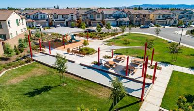 Elevated view of a neighborhood park with square play area with large shade connected by concrete pathways to a seating area with picnic tables next to a bocce ball court. 