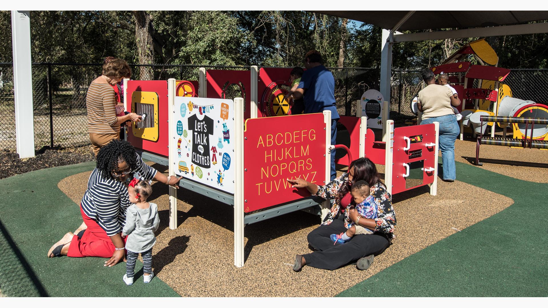 Teachers help young children learn and play at play panels making up a small play structure. 