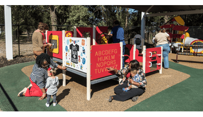 Teachers help young children learn and play at play panels making up a small play structure. 