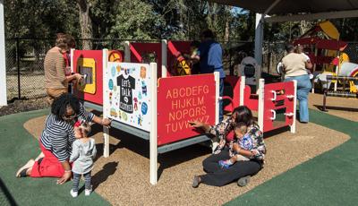 Teachers help young children learn and play at play panels making up a small play structure. 