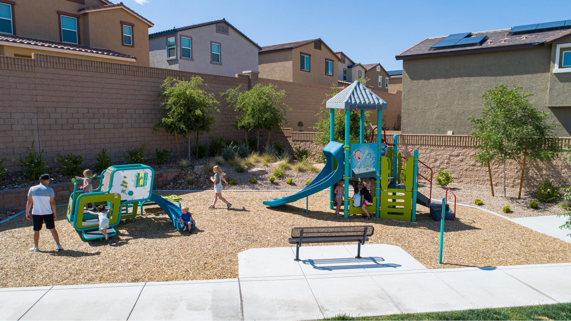 Children play at a small neighborhood park with a science themed play structure for older children with a matching color themed smaller play structure for toddlers.