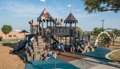 School aged children wearing school uniforms playing on castle-themed playground. Play space also includes a dragon themed playground. 