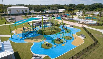 A playground filled with children designed with a pond theme showcasing lilly pads, fish, and nature all next to a nature themed splash pad. 