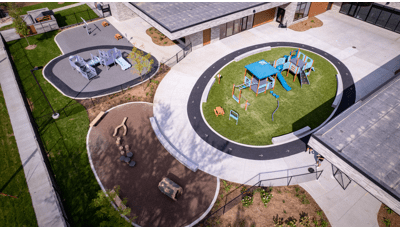 Elevated view of a school building with two separate circular play areas with one structure for toddlers while the other is for a bit older children.