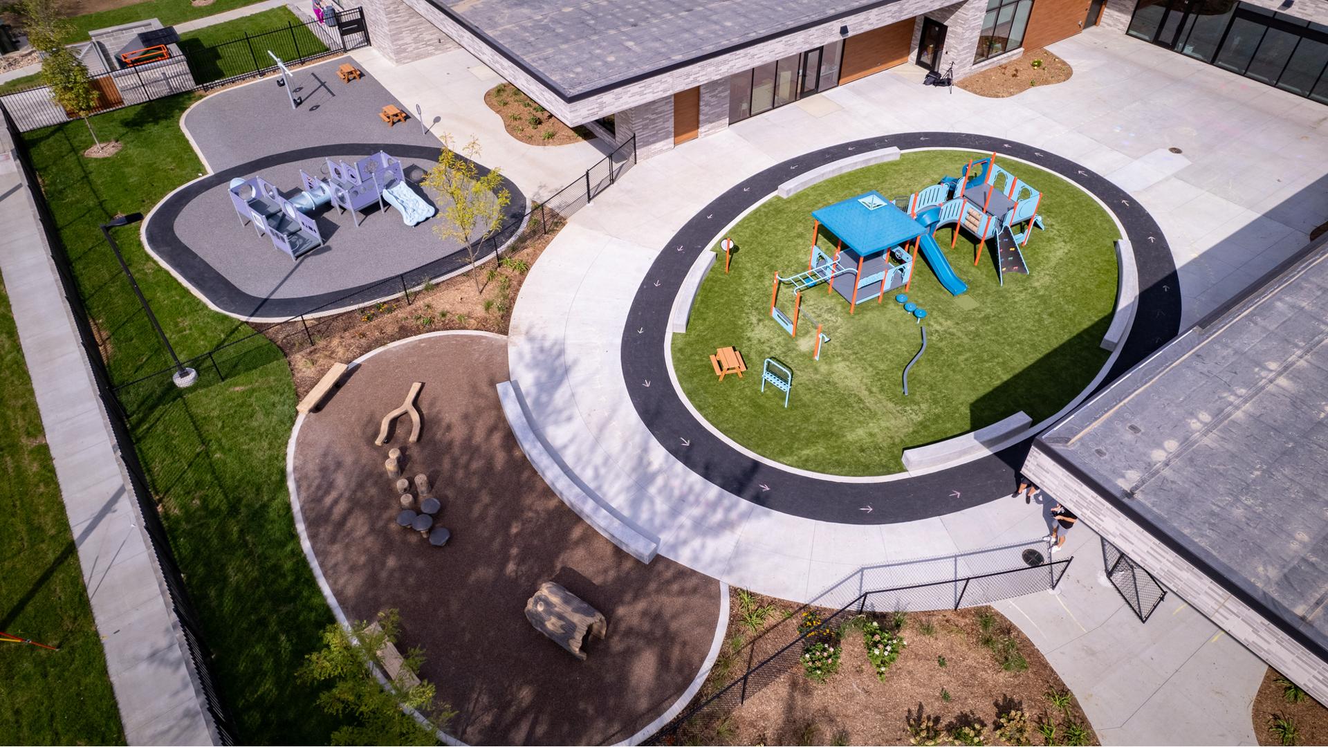 Elevated view of a school building with two separate circular play areas with one structure for toddlers while the other is for a bit older children.