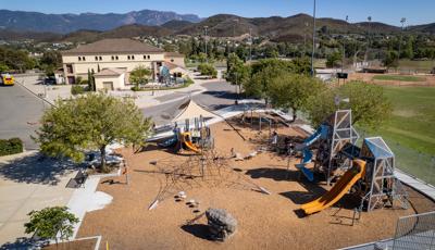 Elevated view of a park playground and an additional play structure across the street in a enclosed area for younger children.